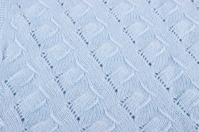 Close-up of a baby-blue cashmere blanket with flowing lace cables and small openwork details.